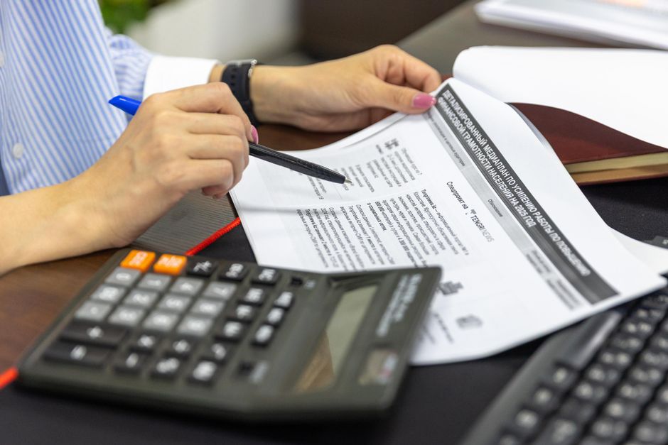 Zatvoreni kadar osobe koja analizira financijske dokumente kalkulatorom i olovkom